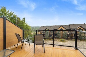 A wooden deck with two chairs, a glass railing, and a view of a row of houses. - 4 Storey Ski In/Out Mountain Home in Tremblant (Mont-Tremblant)