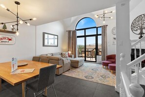 Een moderne woonkamer met een groot raam, een eethoek met een houten tafel en een trap.