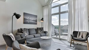 A modern living room with a grey sofa, two armchairs, a round coffee table, and a large window with curtains. - 4 Storey Ski In/Out Mountain Home in Tremblant (Mont-Tremblant)