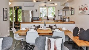 A modern kitchen with a central island, stainless steel appliances, and a dining area with white chairs and a wooden table. - 4 Storey Ski In/Out Mountain Home in Tremblant (Mont-Tremblant)