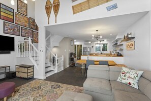 A modern living room with a grey sofa, a patterned rug, a staircase, and a kitchen area with a wooden countertop. - 4 Storey Ski In/Out Mountain Home in Tremblant (Mont-Tremblant)