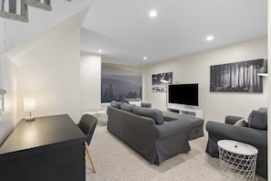 A modern living room with a sofa, a TV, and artwork on the wall. - 4 Storey Ski In/Out Mountain Home in Tremblant (Mont-Tremblant)