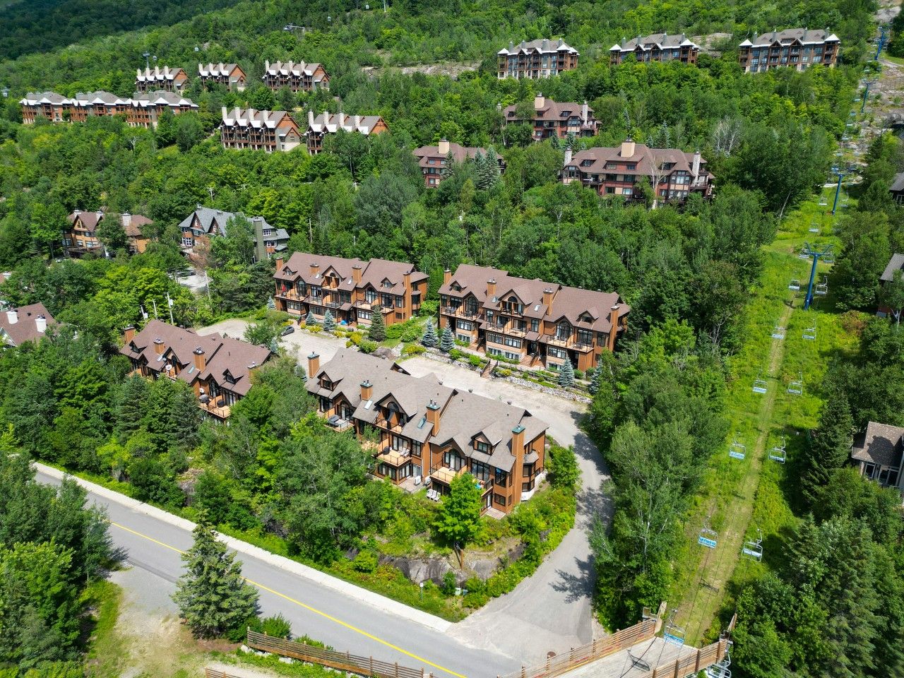 A resort with multiple chalet-style buildings, a ski lift, and a road.