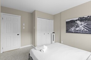 A bedroom with a bed, two white doors, a wall-mounted heater, and a framed picture. - 4 Storey Ski In/Out Mountain Home in Tremblant (Mont-Tremblant)