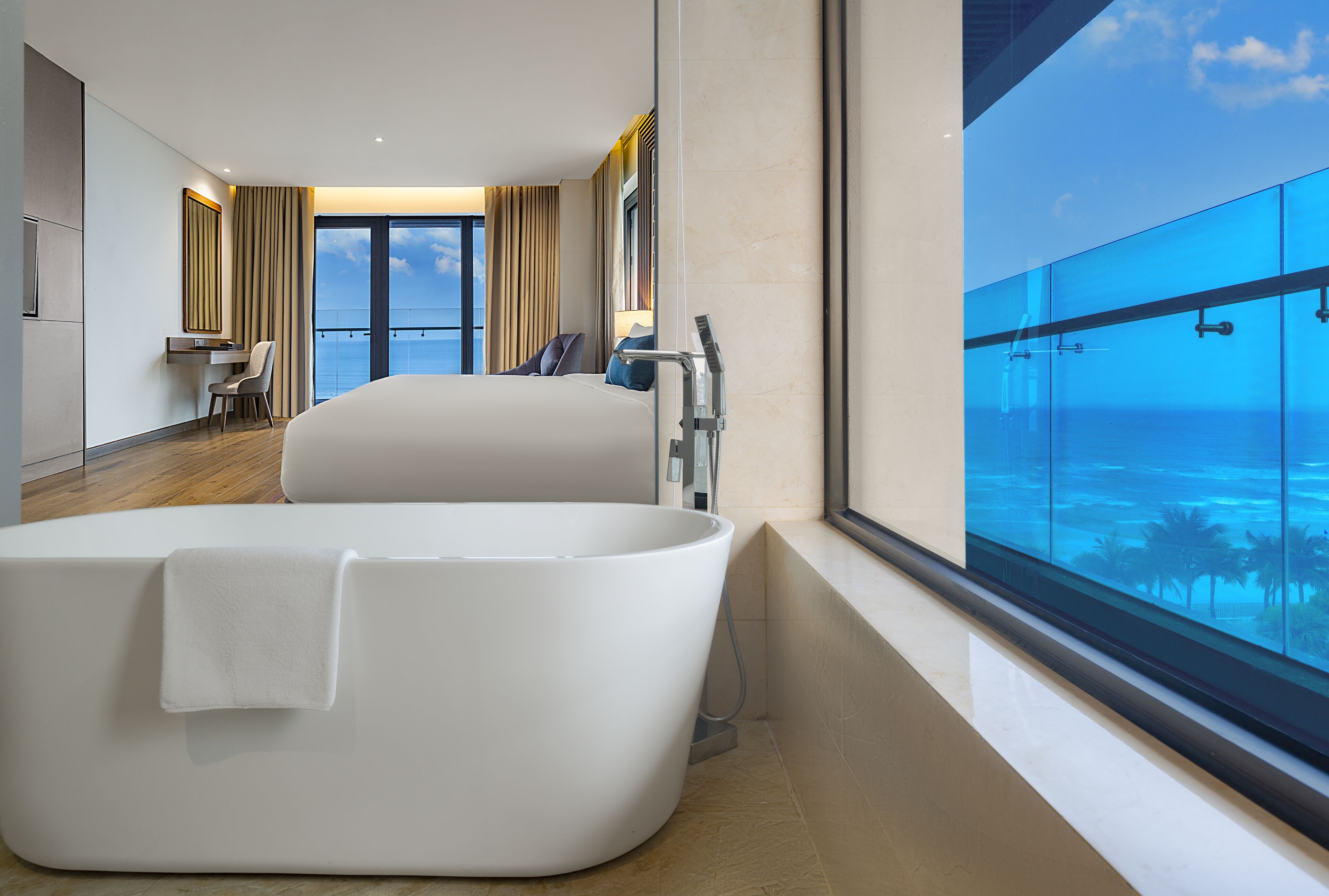 A modern hotel room with a large bathtub, a desk, and a view of the ocean.