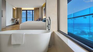 A modern hotel room with a large bathtub, a desk, and a view of the ocean.