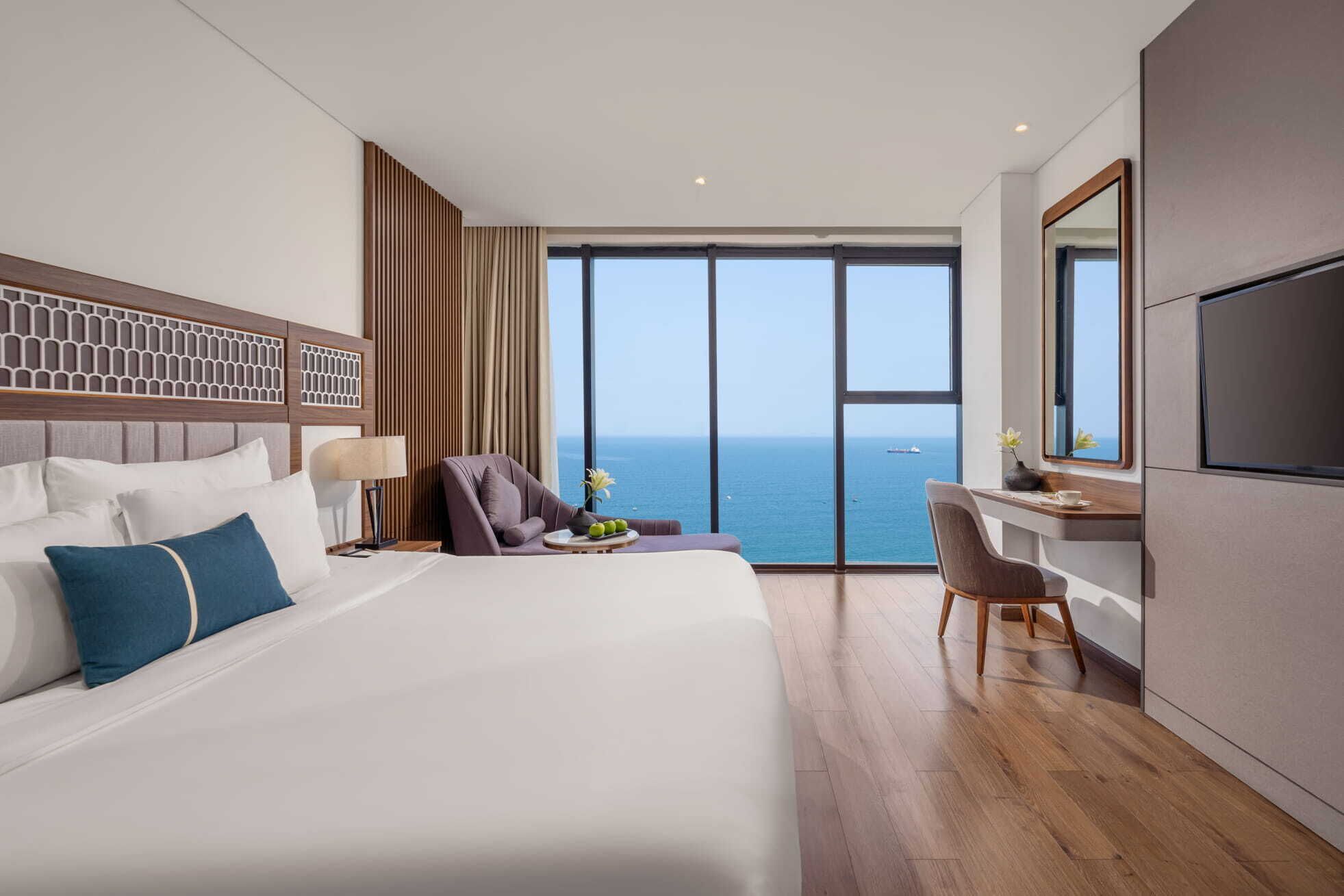 Une chambre d’hôtel moderne dotée d’un grand lit, d’un bureau avec une chaise, d’une télévision et offrant une vue sur la mer.