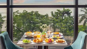 A dining table with a variety of dishes and two chairs, set against a backdrop of a sunset view through large windows. - Peninsula Hotel Danang (Da Nang)