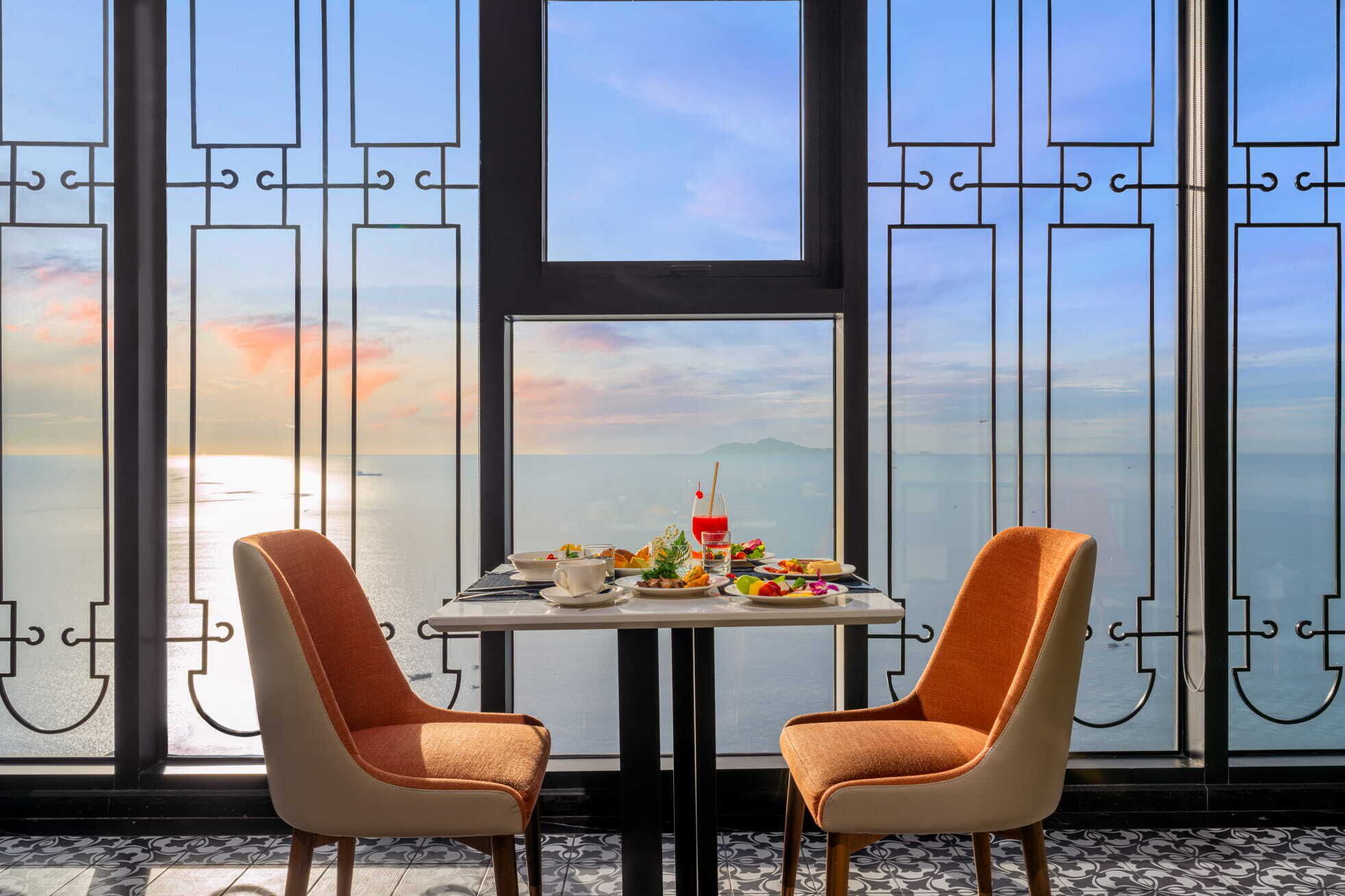 A dining area with a table set for two, overlooking a scenic view of the sea and mountains.