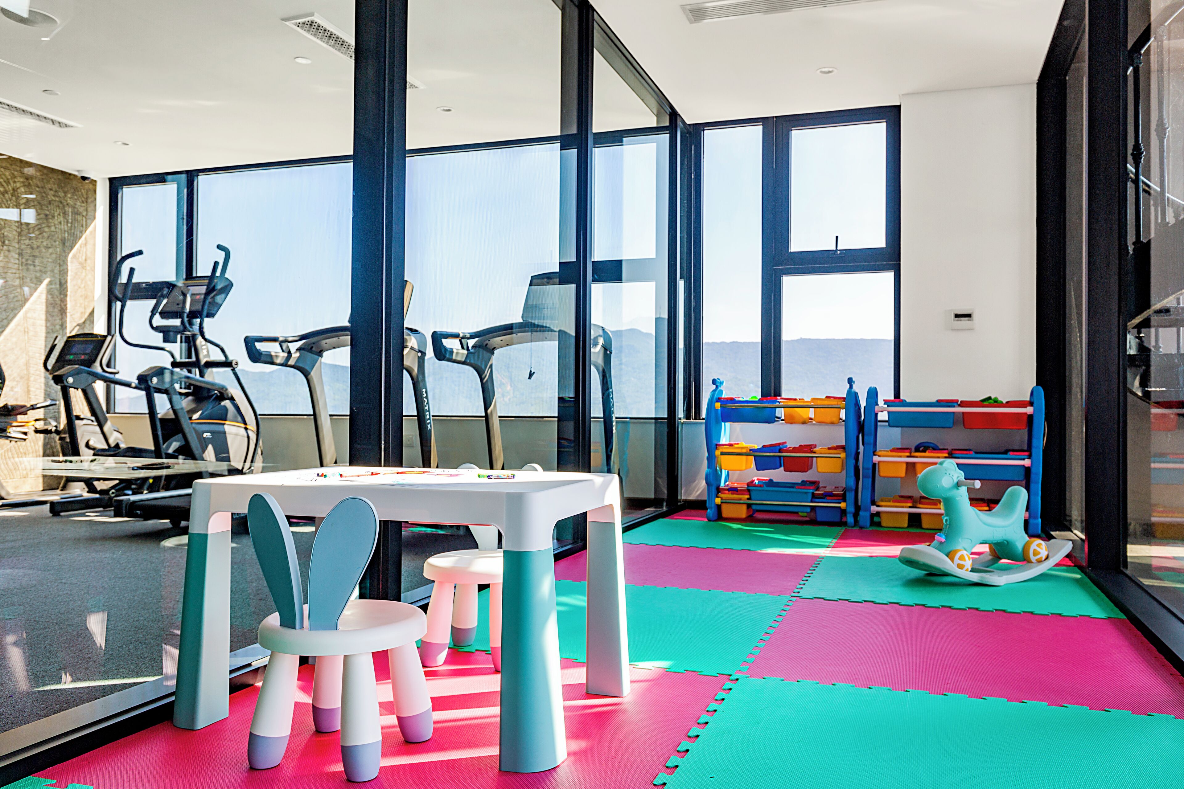 A fitness room with exercise equipment, a table with chairs, and colorful play mats.