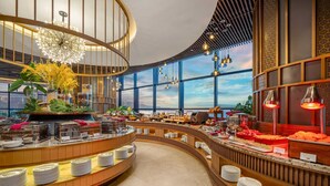 A modern breakfast buffet with a curved layout, large windows, and decorative lighting.