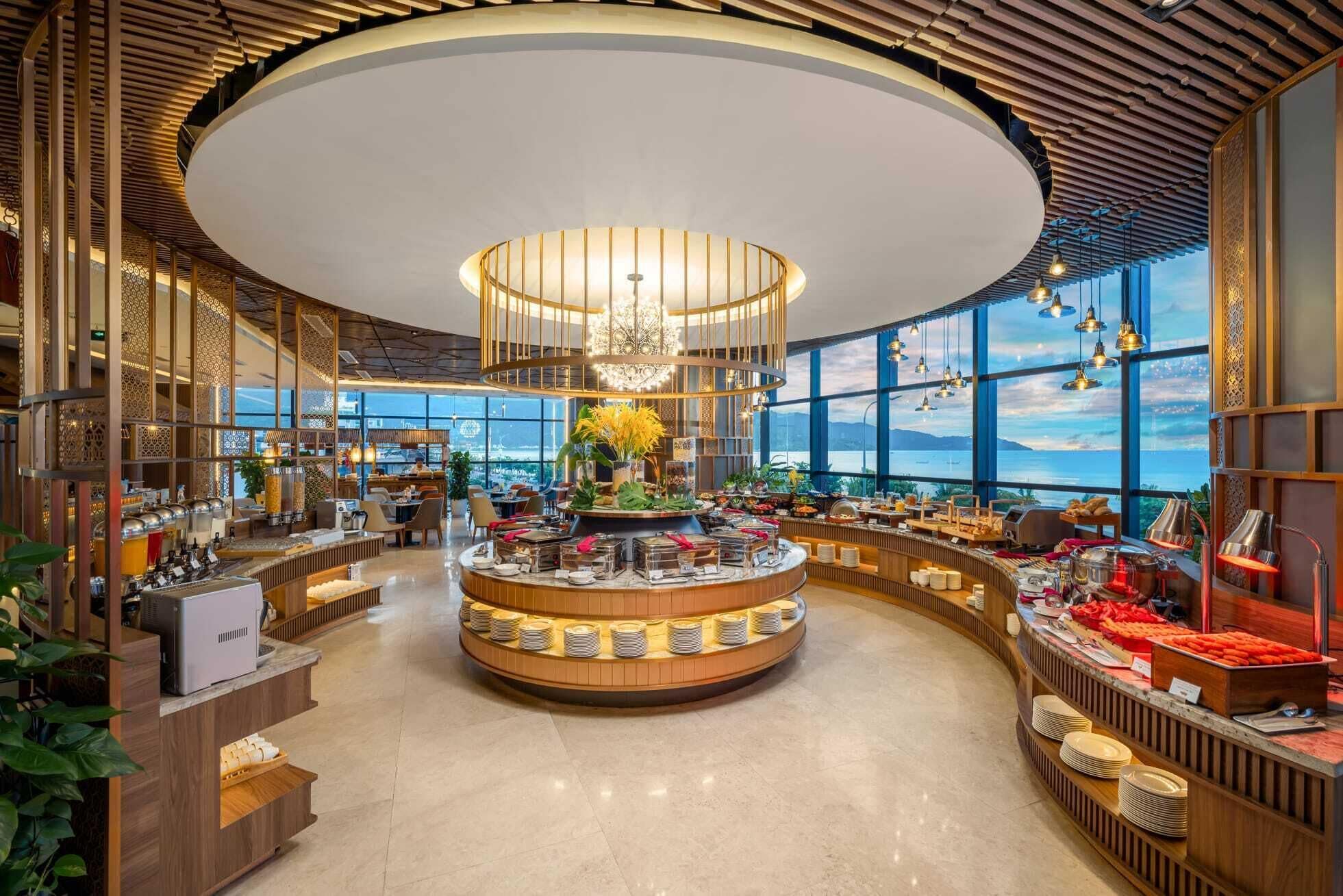 A spacious, modern dining area with a central circular bar, large windows offering views, and a high ceiling with a unique light fixture.