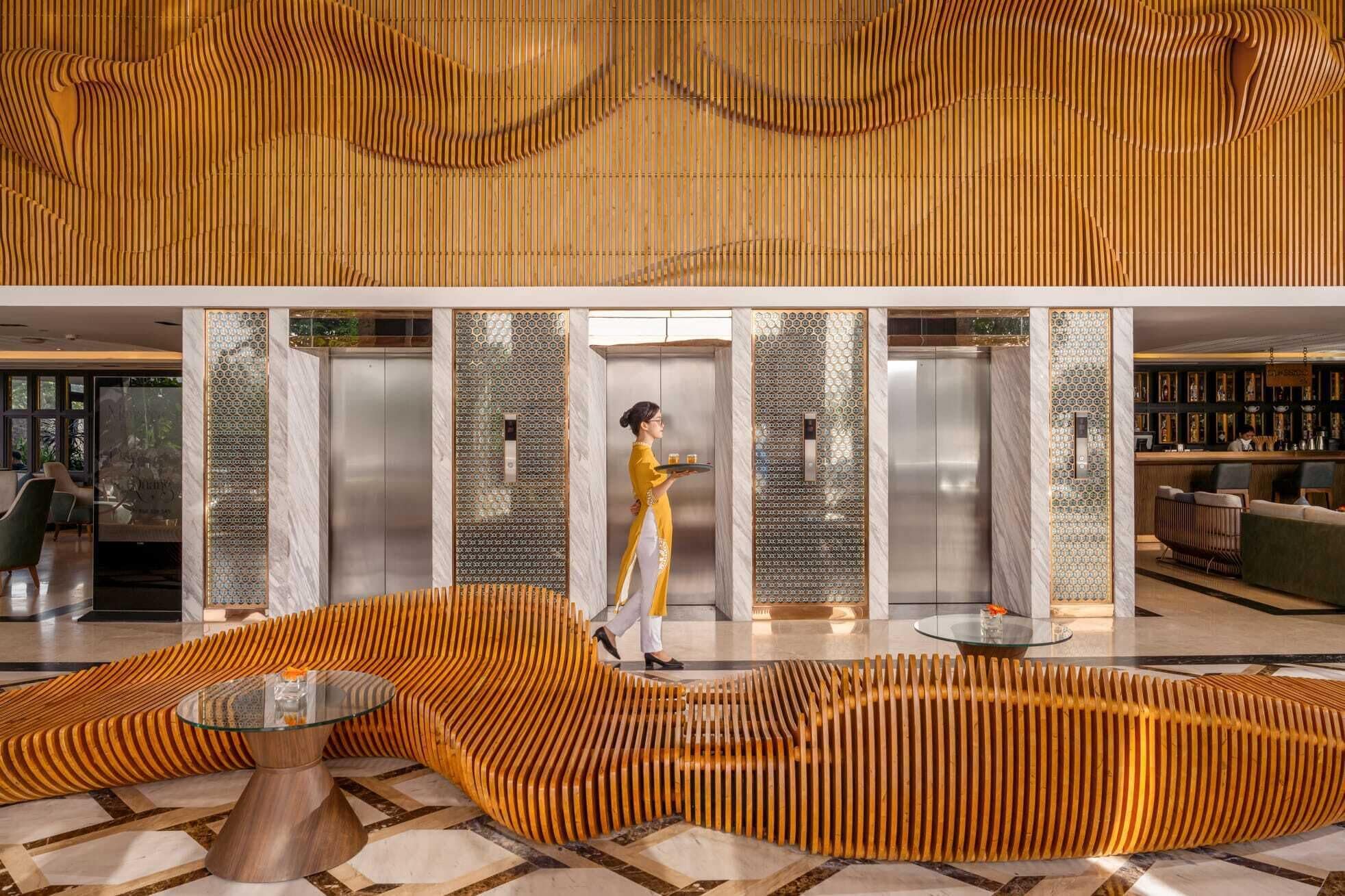 A modern lobby with a unique wooden wave design, elevators, and a bar area.