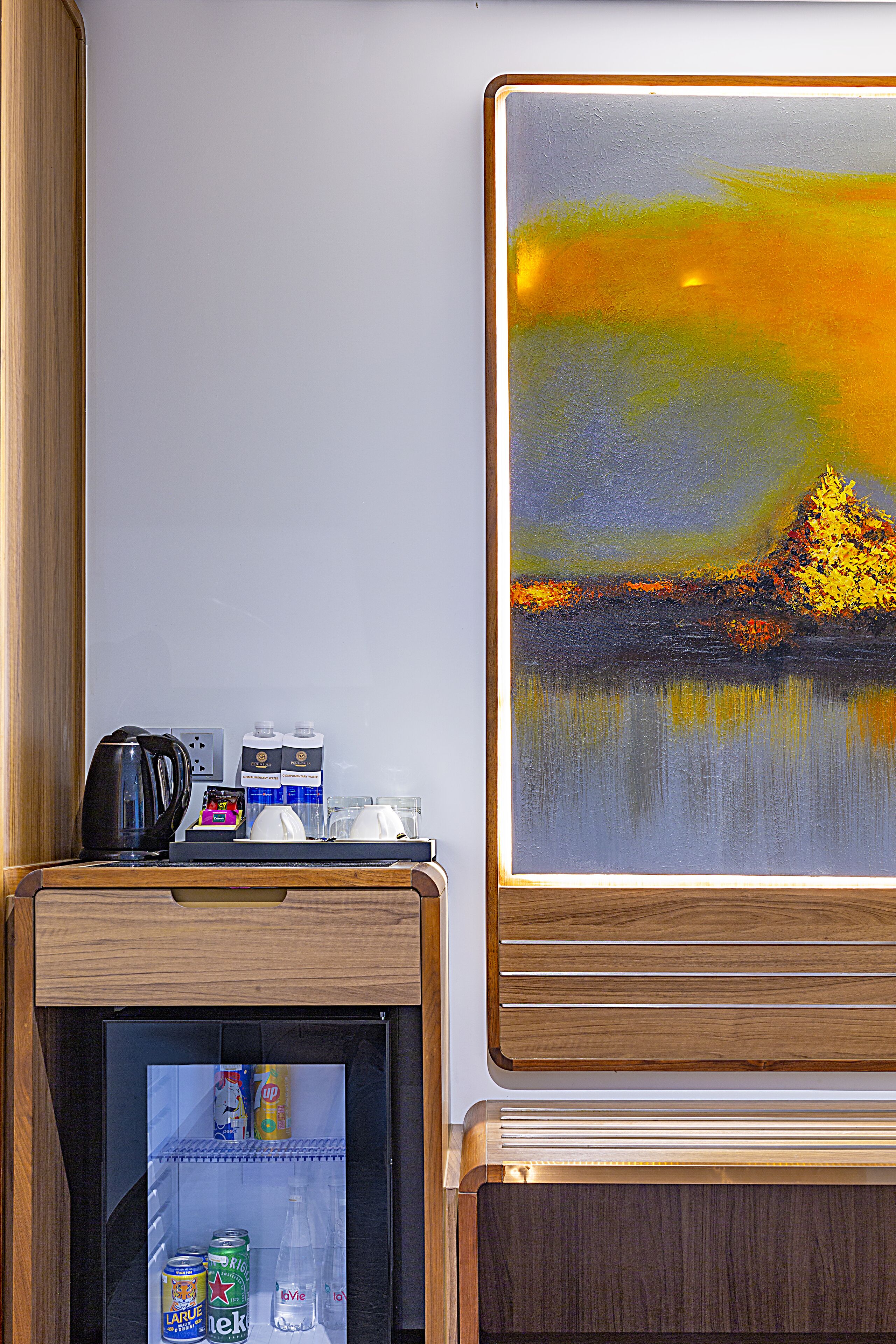 Un minibar con un cuadro de un atardecer sobre el agua, una tetera y agua embotellada.