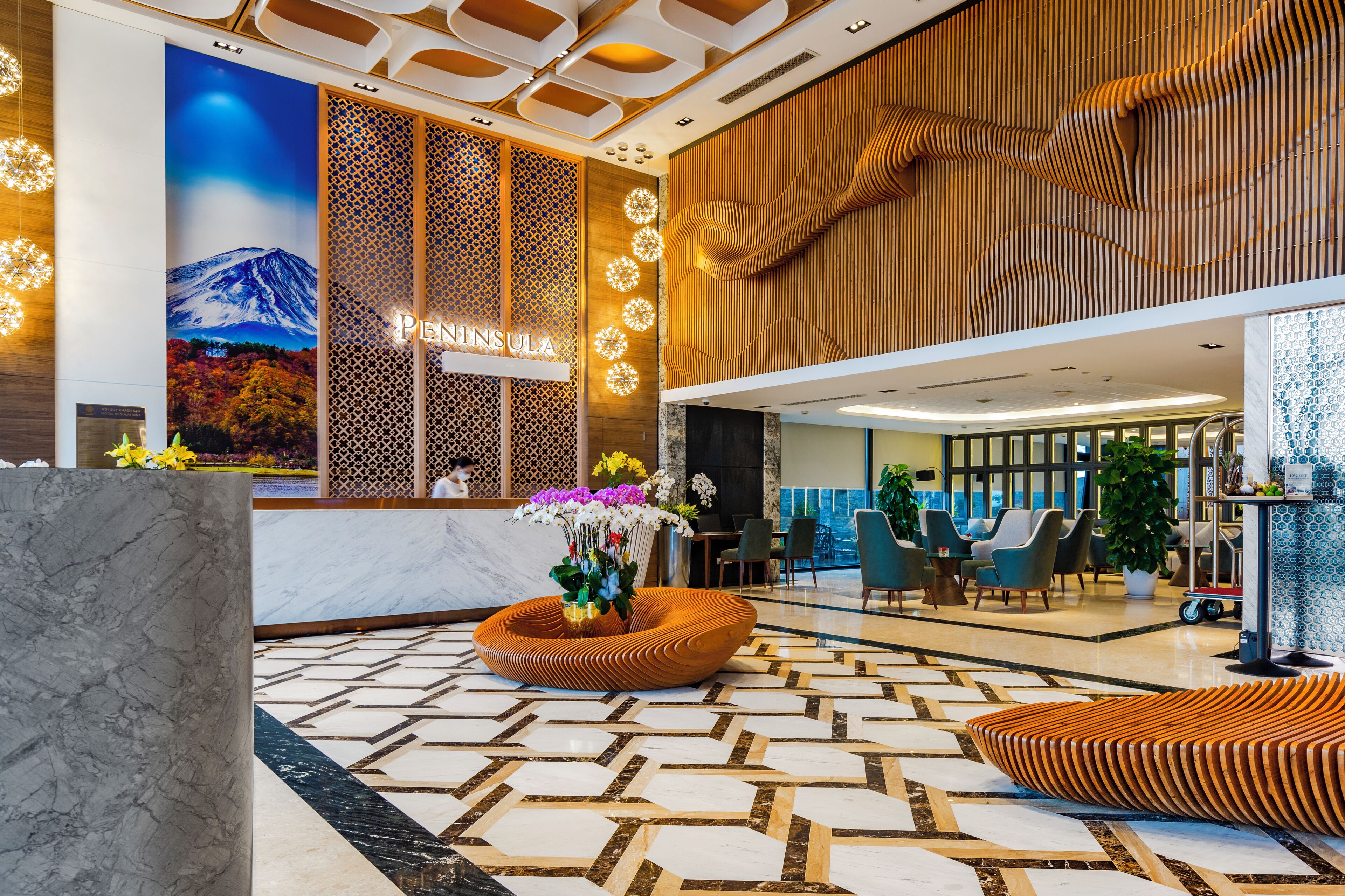A modern hotel lobby with a reception desk, a large wall mural, and a patterned floor.