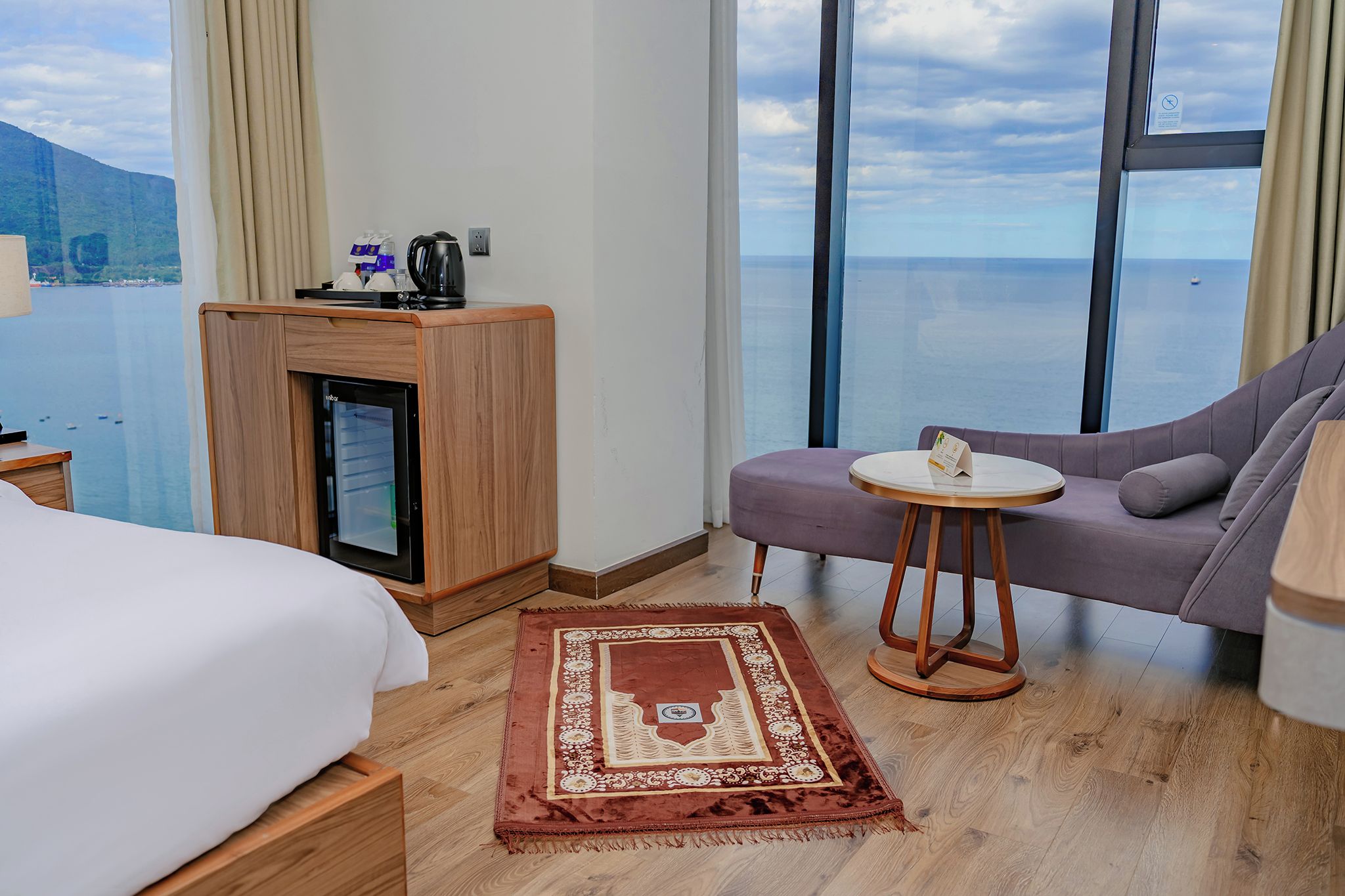 Habitación de hotel con cama, sofá, una mesita, cafetera y vista al mar.