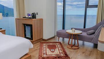Habitación de hotel con cama, sofá, una mesita, cafetera y vista al mar.