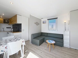 A compact living space with a kitchenette, a dining table, a sofa, a small round table, and a window with a view.