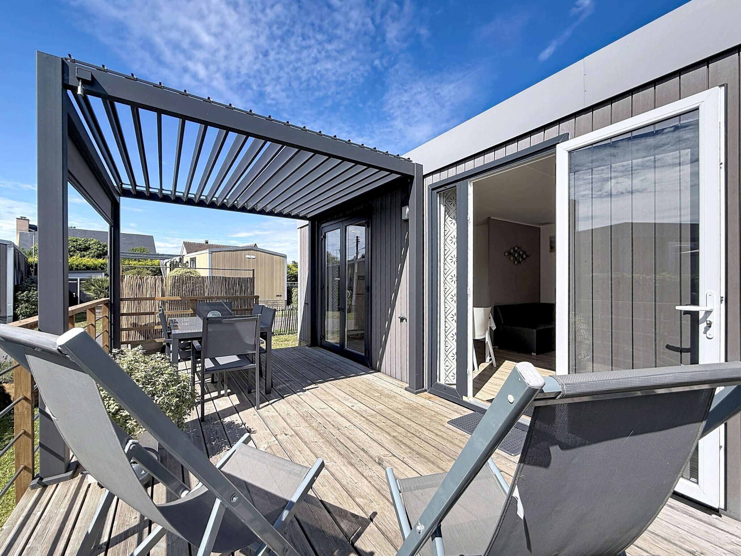 A modern outdoor patio with a wooden deck, metal chairs, and a glass door leading to an interior space.