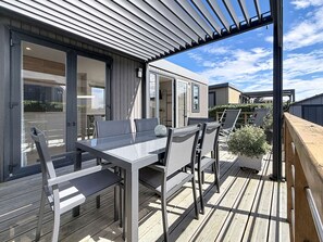 An outdoor deck with a table and chairs, a pergola, and a view of a modern building.