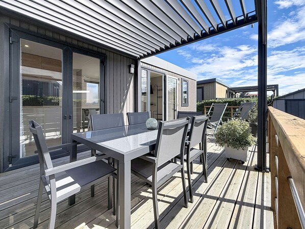An outdoor deck with a table and chairs, a pergola, and a view of a modern building.