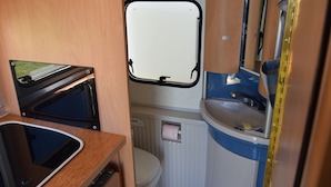 A compact bathroom with a toilet, sink, and window. - Caravan rental region Guidel(56520) (Guidel)
