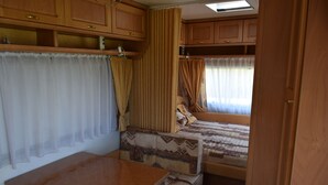 A compact RV interior with a bed, a table, and a kitchenette area. - Caravan rental region Guidel(56520) (Guidel)
