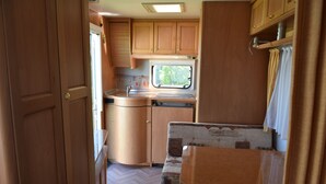 A compact RV kitchen with wooden cabinets, a window, and a sink. - Caravan rental region Guidel(56520) (Guidel)