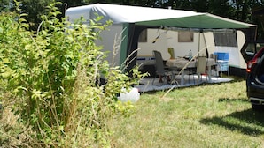 A camping site with a covered RV and a table set up for dining. - Caravan rental region Guidel(56520) (Guidel)