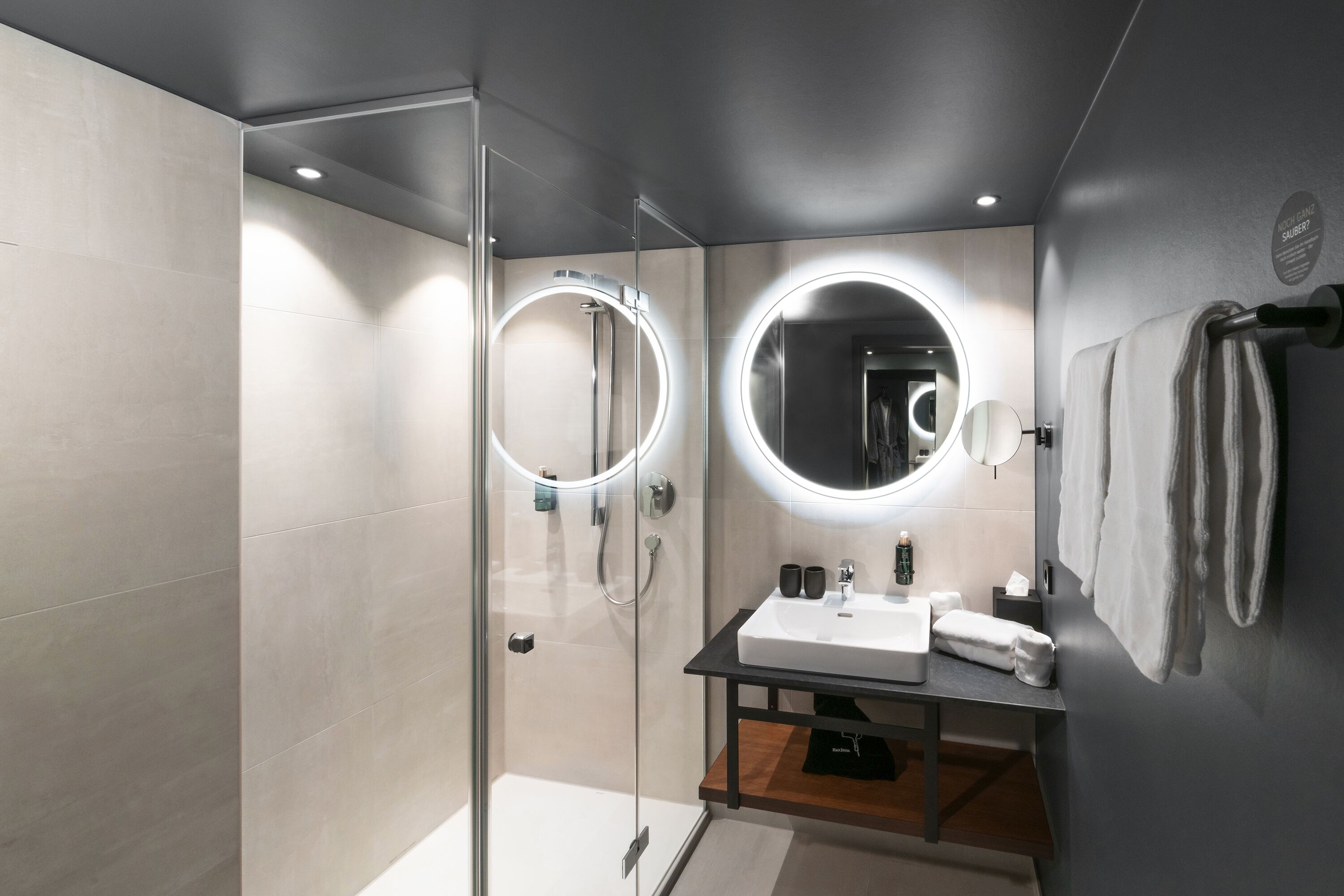 A modern bathroom with a glass-enclosed shower, a vanity with a sink, and two illuminated mirrors.