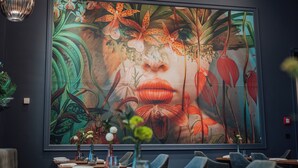 Un restaurante con un gran mural floral en la pared, mesas dispuestas con platos y vasos, y un diseño de techo moderno.