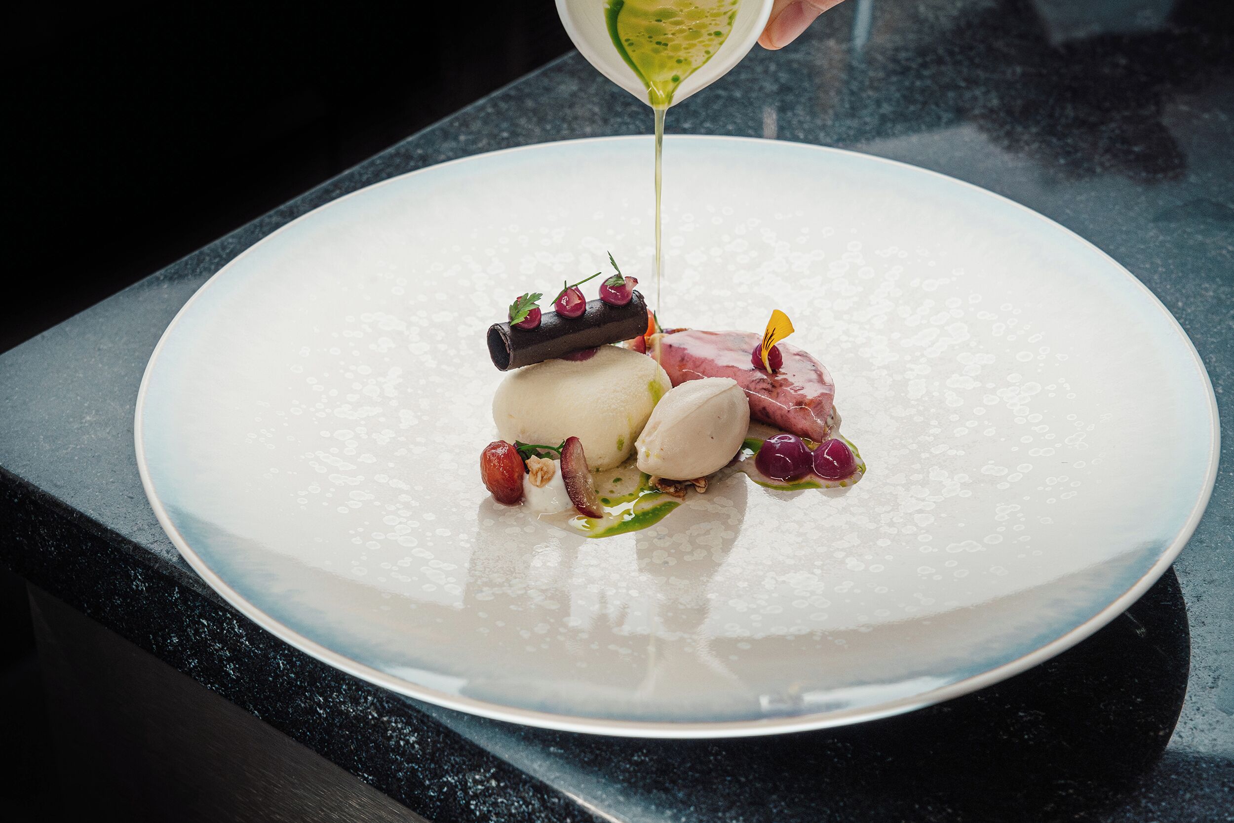 A dessert plate with various food items and a sauce being poured.