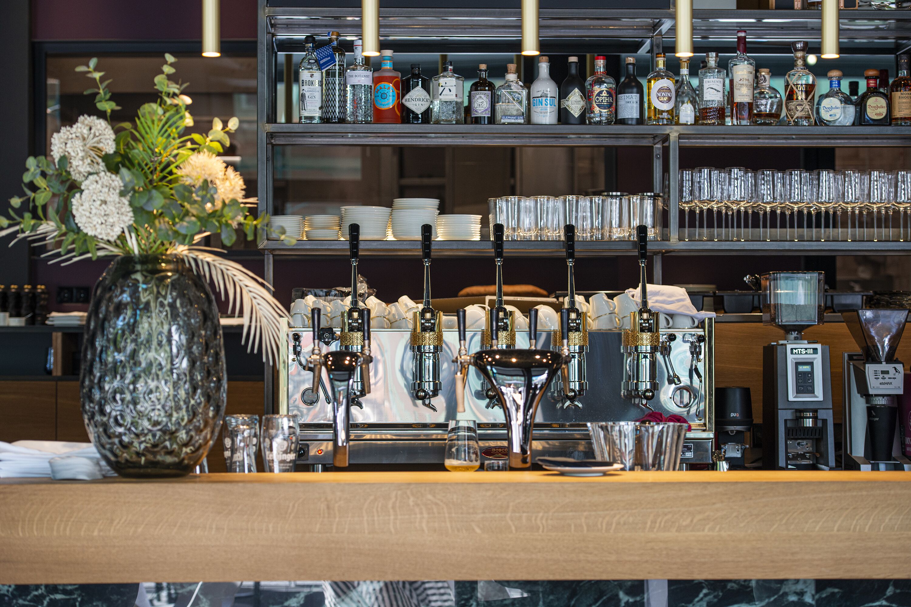 A bar area with multiple taps, shelves of bottles, and a vase with flowers.