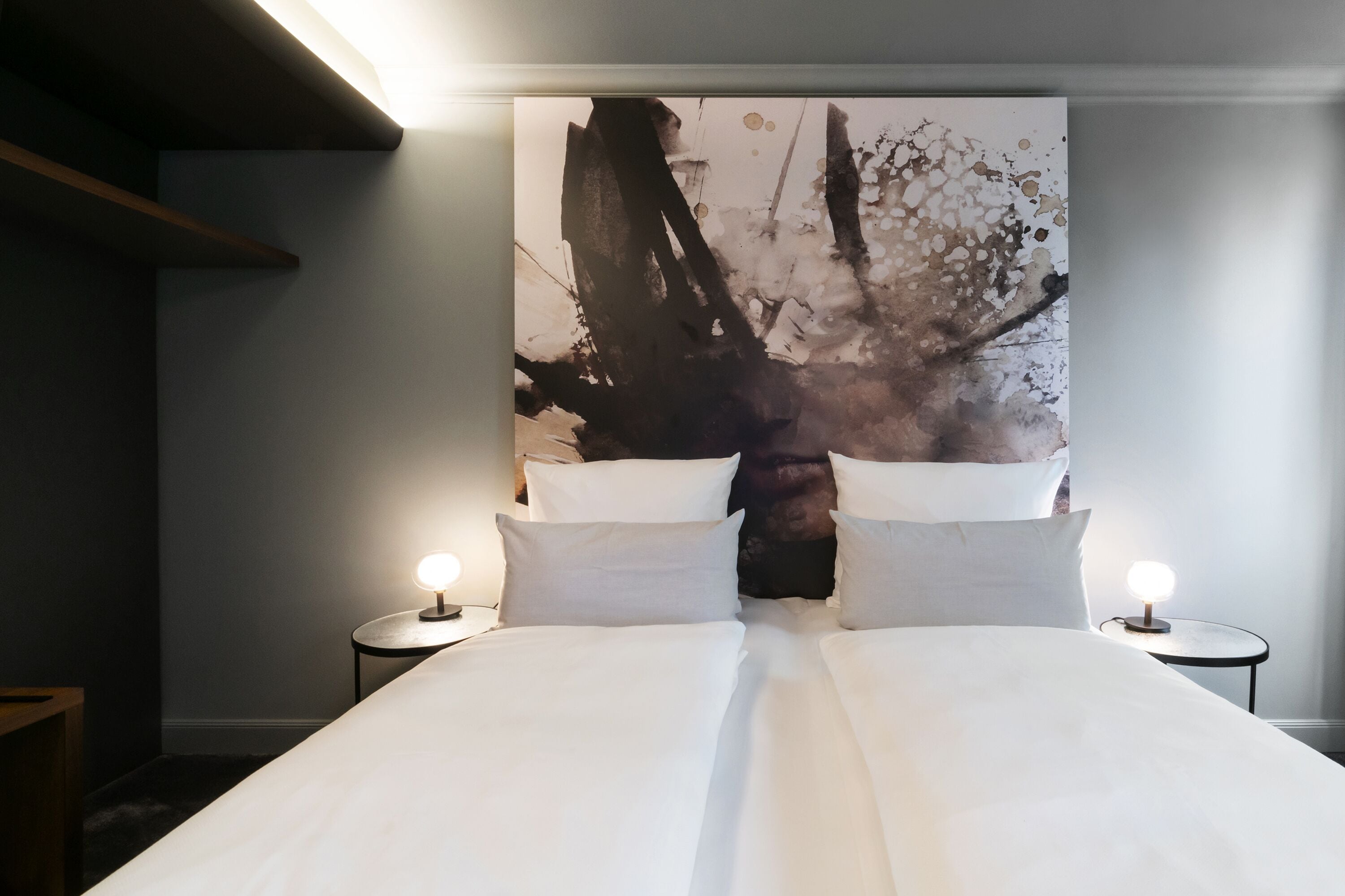 A bed with white linens, two bedside tables with lamps, and a large abstract painting on the wall.