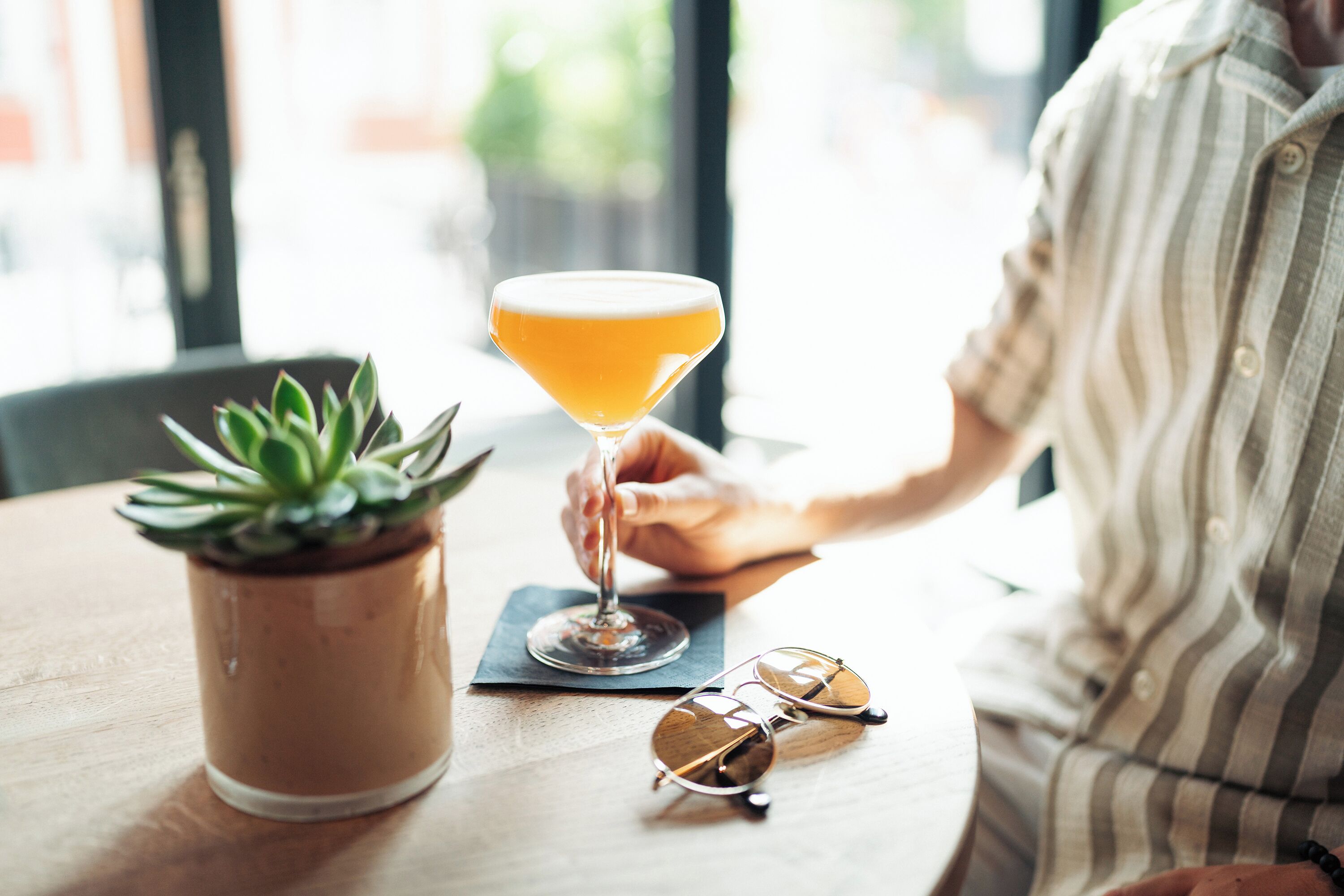 A person sitting at a table with a martini glass and a potted plant.