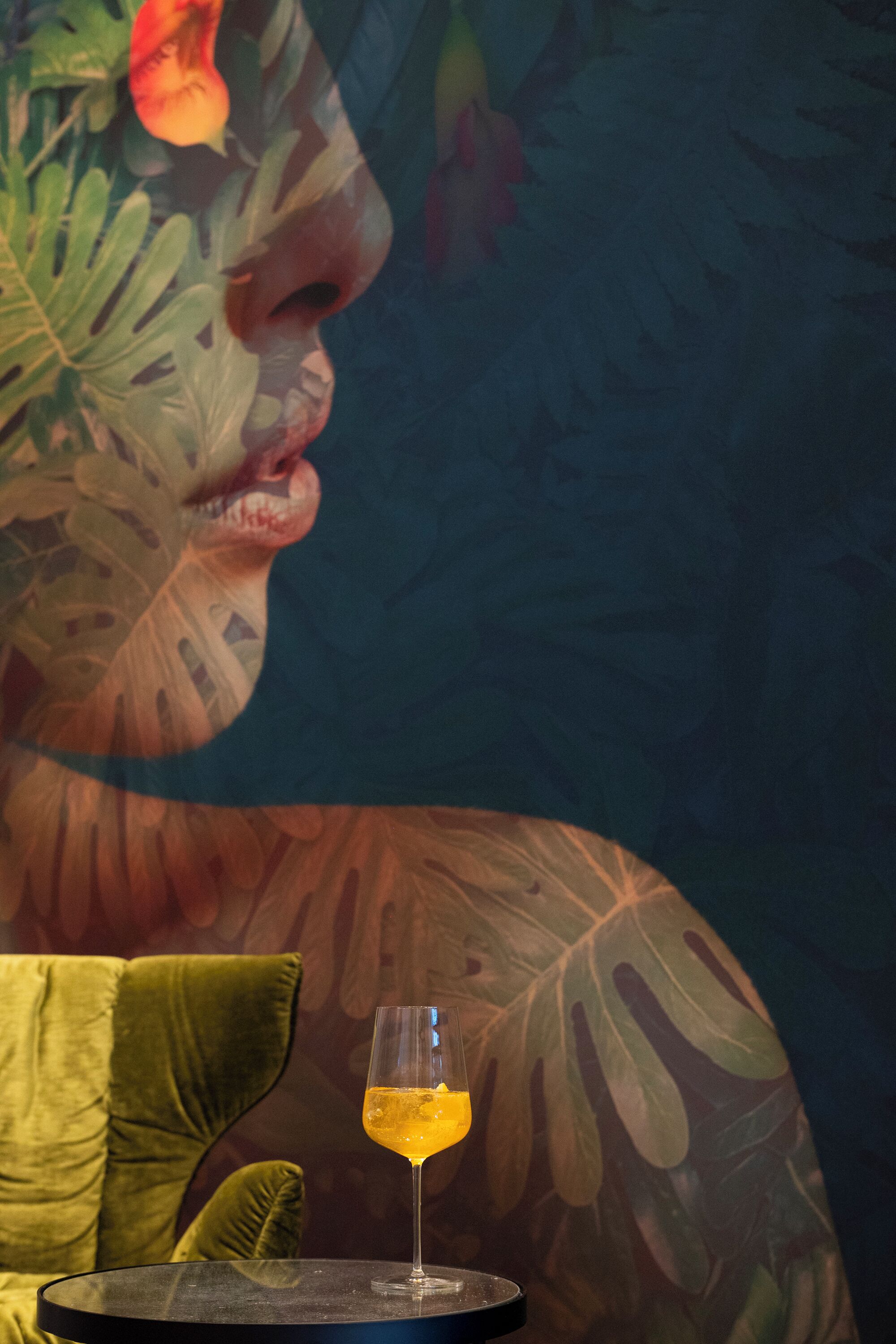 A glass of drink on a table with a tropical mural in the background.
