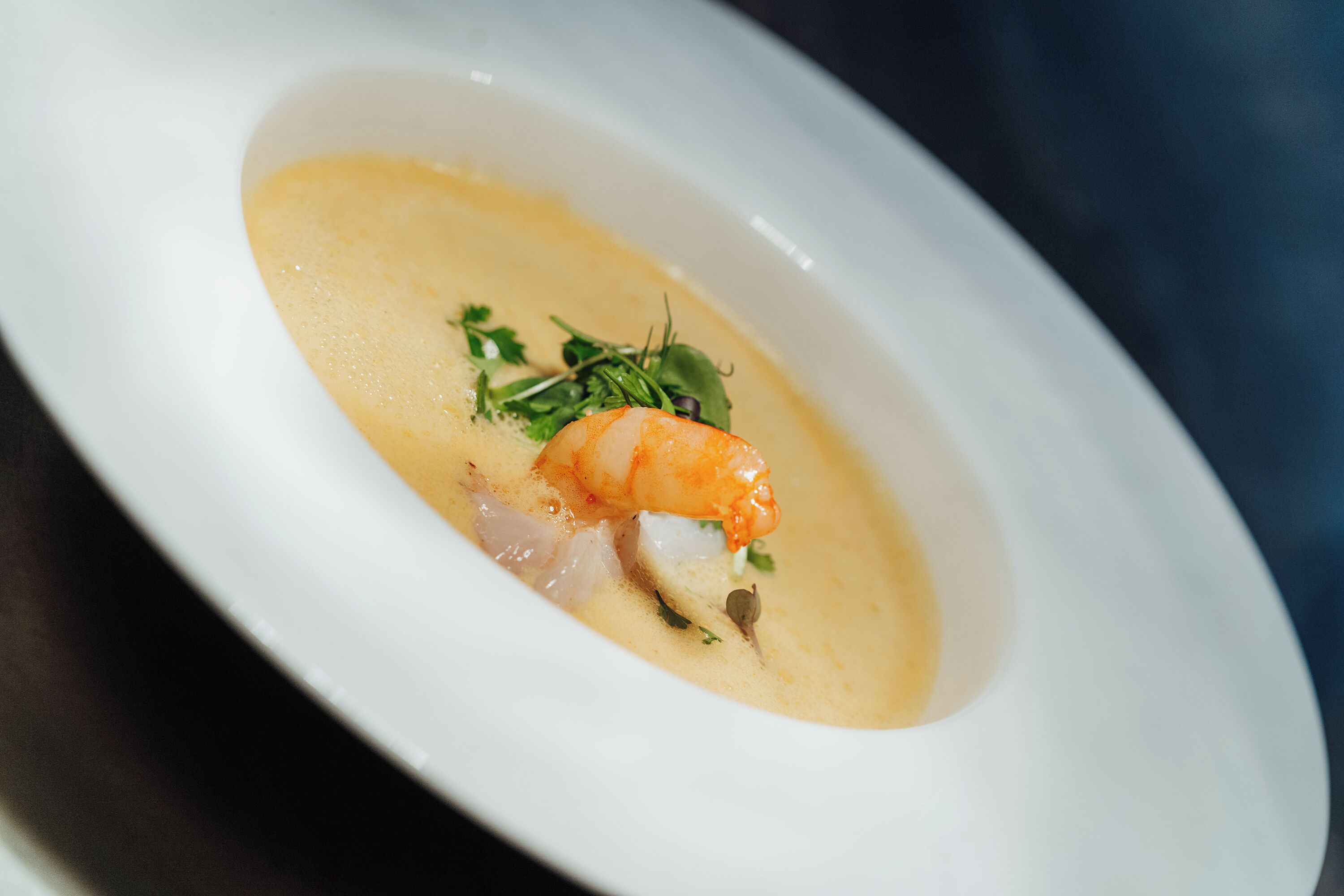 A white oval dish containing a seafood dish with a shrimp, white fish, and greens.