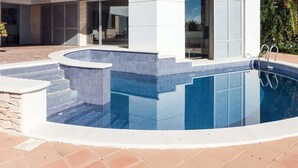 Una casa moderna de dos pisos con piscina, ventanas amplias y un detalle en rojo.