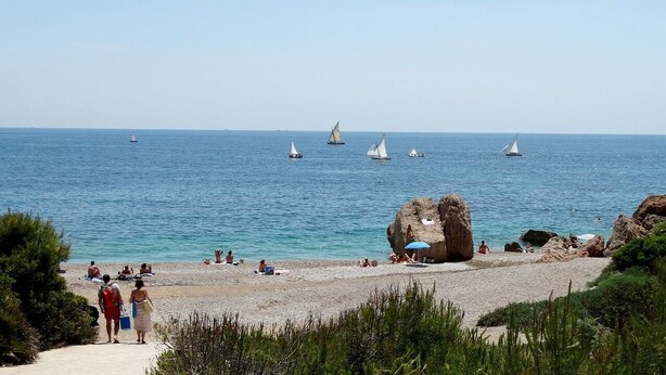 Una playa con gente tomando el sol y una gran formación rocosa.