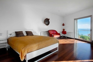A modern bedroom with a large bed, a red chair, and a view of the sea. - LA MEVA LLUNA, Luxury villa on the beachfront with pool (L'Ampolla)