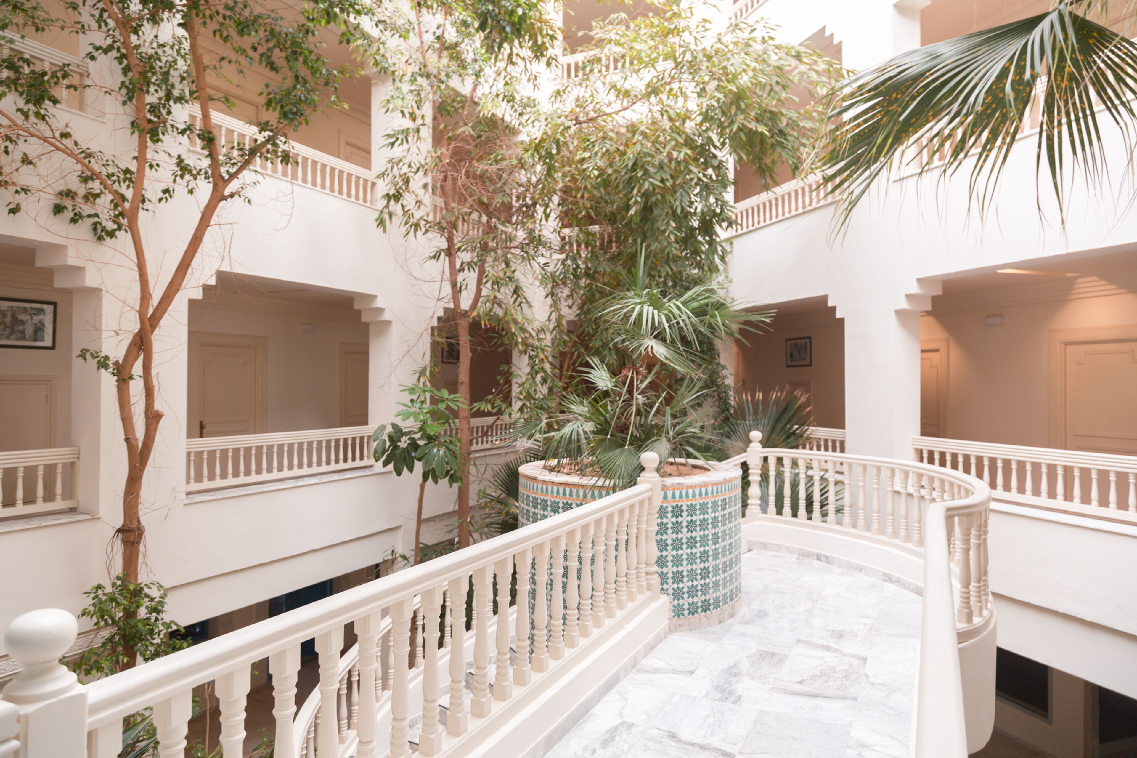 A multi-level courtyard with white balustrades, potted plants, and a marble floor.