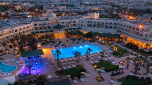 Un hotel con una amplia piscina central, varias zonas de descanso y un patio bien iluminado.