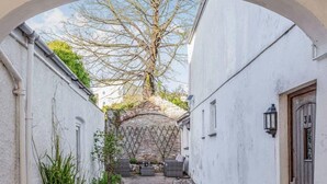 A narrow alleyway with a stone wall, a wooden door, and a small garden area with plants and a bench. - Lovely Villa 1 Double 1 Double Sofa 6 Single,1bunk (Torquay)