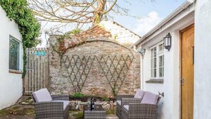 A courtyard with wicker furniture, a stone wall, and a wooden door. - Lovely Villa 1 Double 1 Double Sofa 6 Single,1bunk (Torquay)