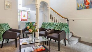 A lobby with two armchairs, a coffee table, and a vase with flowers. There is a staircase with a wooden handrail and a painting on the wall. - Lovely Villa 1 Double 1 Double Sofa 6 Single,1bunk (Torquay)