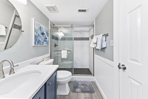 Un bany amb dutxa tancada amb vidre, un lavabo blanc, un vàter i una obra d'art blava a la paret.