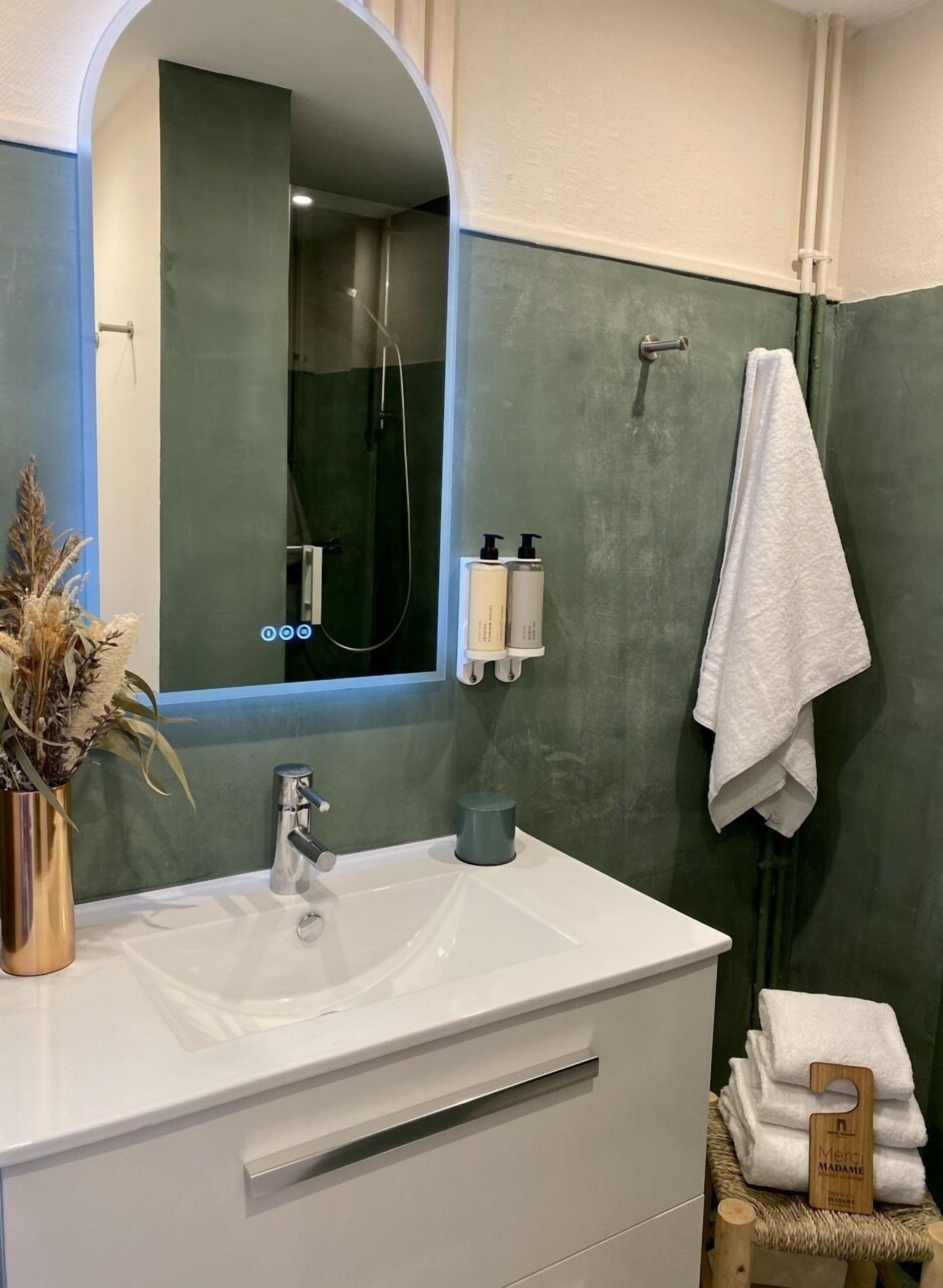 A bathroom with a white sink, a mirror, a shower, and a towel rack.