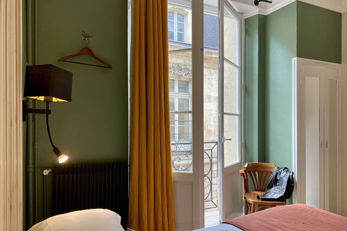 A room with a bed, a chair, a hanging coat rack, and a window with curtains.