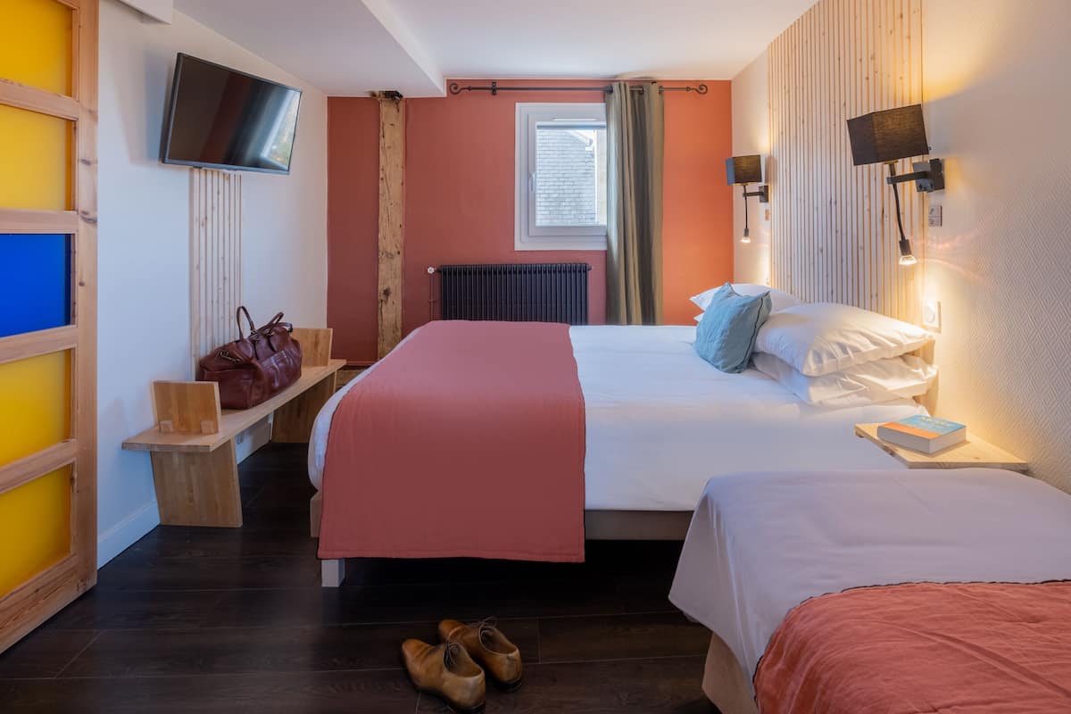 A hotel room with two beds, a TV, a window with curtains, and a bench with a handbag.