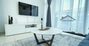 A modern living room with a white TV, a round coffee table, and a grey sofa. - Casa Grand one-bedroom duplex apartment (Accra)